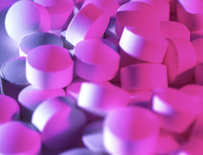 Een stapel witte tabletten ligt verspreid, verlicht door een levendig paars en roze licht, wat een kleurrijk contrast creëert.
