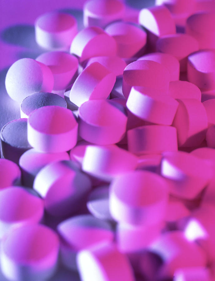 Een stapel witte tabletten ligt verspreid, verlicht door een levendig paars en roze licht, wat een kleurrijk contrast creëert.