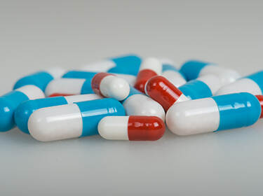 Een verspreide stapel capsules op een oppervlak, met een mix van blauwe en witte, en rode en witte capsules. De capsules zijn van uniforme grootte, met een glanzend uiterlijk, wat suggereert dat het medicinale pillen zijn.