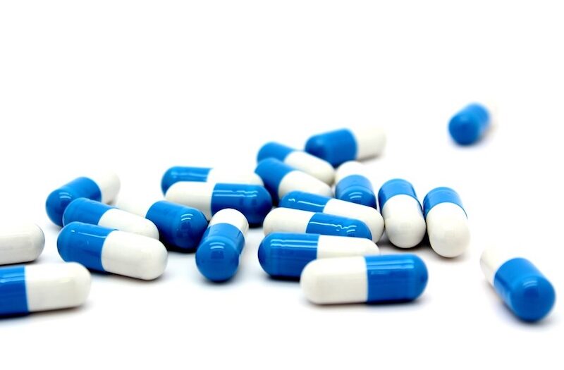 Een verspreide stapel blauwe en witte capsules op een witte achtergrond.