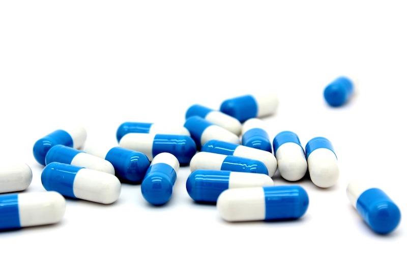 Een verspreide stapel blauwe en witte capsules op een witte achtergrond.